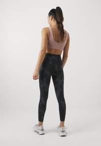 Conjunto atlético composto por um soutien desportivo suave e rosa claro e leggings pretas de cintura alta com um padrão de camuflagem subtil. Ténis com sola de borracha.