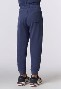 Pantaloni jogger blu navy realizzati in materiale morbido, con una cintura elastica, polsini alle caviglie e un dettaglio della tasca posteriore. Indossati con scarpe sportive.