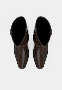 Ζευγάρι στιλβωμένων καφέ σκούρων δερμάτινων μποτών αστραγάλου με τετράγωνες μύτες και διακοσμητικές λουρίδες, φαινομένων από πάνω σε λευκό φόντο.