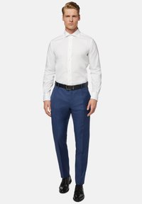 Witte lange mouwenshirt met een puntige kraag, gecombineerd met blauwe broeken en een zwarte riem, gedragen met zwarte nette schoenen.