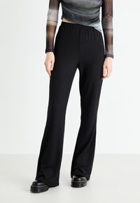 Pantalons noirs évasés en tissu texturé à côtes, avec une taille élastique, associés à des bottes plates-formes noires imposantes.