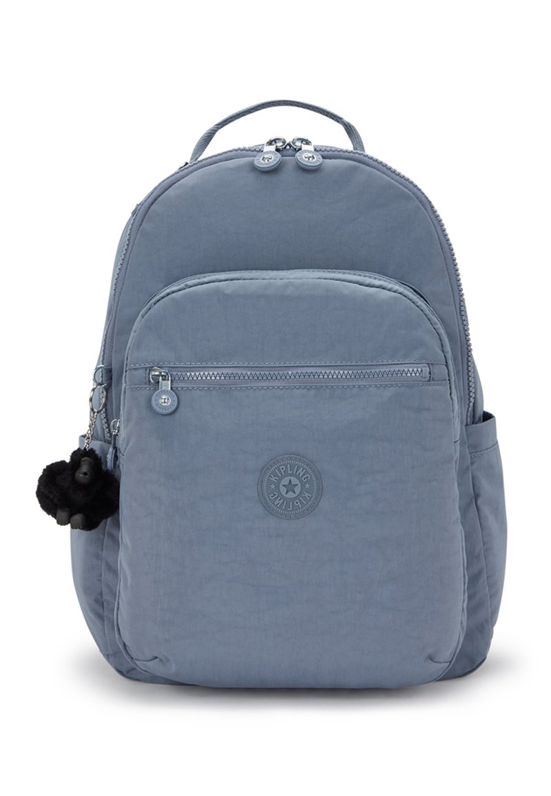 Světle modrý batoh z měkké tkaniny s zaobleným tvarem. Má přední kapsu, zipové uzávěry a černou opičí klíčenku.