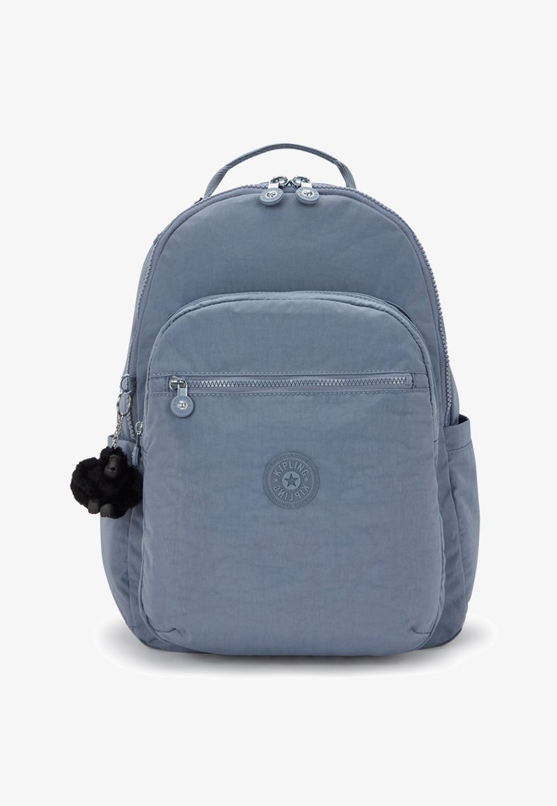 Světle modrý batoh z měkké tkaniny s zaobleným tvarem. Má přední kapsu, zipové uzávěry a černou opičí klíčenku.