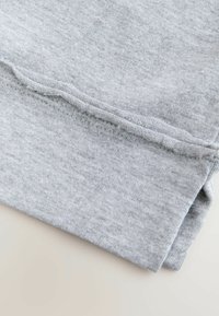 Tejido de sudadera gris, textura suave con un patrón ligeramente jaspeado. Presenta una costura a lo largo del borde y un dobladillo doblado.