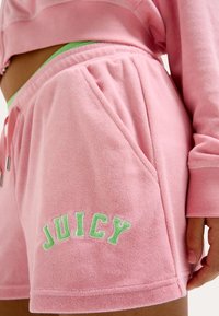 Shorts en éponge roses avec poches avant, ornés de lettres brodées "JUICY" en vert. Texture douce et coupe décontractée pour un confort optimal.