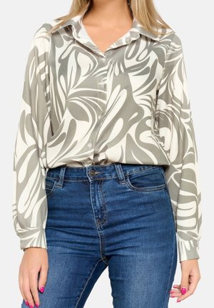 Kvinde iført en langærmet skjorte med abstrakte grå og hvide mønstre, stukket ned i højtaljede blå jeans.