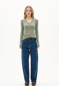 Långärmad, ribbad, olivgrön topp, kombinerad med lösa, blå denimbyxor och klackar med leopardmönster, samt ett svart bälte.