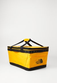 Dzeltens taisnstūra mīkstais aukstuma maisiņš ar melniem akcentiem, divām melnām nesējķermeņiem un The North Face logotipu uz sāniem.