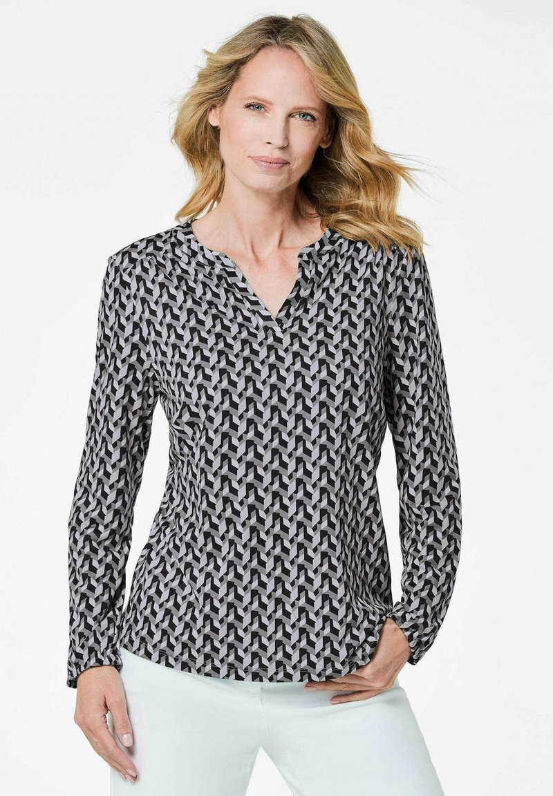 Langärmlige Bluse mit einem schwarz-weißen geometrischen Muster, V-Ausschnitt und Raffung an den Schultern.