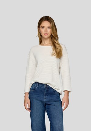 Pull en maille gaufrée blanche avec un col rond et des manches trois quarts, associé à un jean en denim bleu au fit classique.