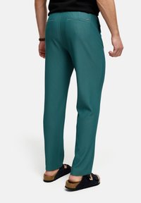 Teal stribede bukser med slim fit, der har baglommer og en glat tekstur, kombineret med sorte slip-on sandaler.