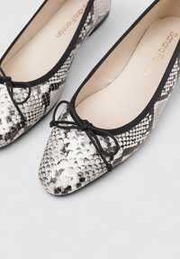 Ballerines à motif serpent noir et blanc avec un bout pointu, bord noir et un nœud noir à l'avant. Doublure intérieure douce.