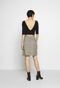 Crop top noir ajusté avec des manches trois-quarts et un décolleté en V prononcé au dos, associé à une jupe en tartan. La mannequin porte des bottines noires.