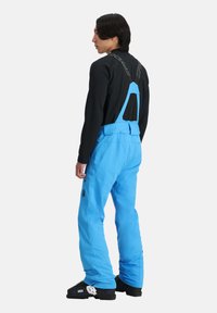 Blaue Schneehosen aus strapazierfähigem Material, ausgestattet mit verstellbaren Trägern, einem Rückenpanel aus Mesh und mehreren Taschen für Funktionalität.