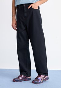 Sorte bredbenede jeans med høj talje, kontrasteret af en lys blå skjorte. Footwear præsenterer et farverigt design med accenter og mønstrede detaljer.