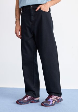 Black wide-leg jeans with a high waist, contrasted by a light blue shirt. Footwear features a colorful design with accents and patterned details.