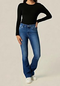 Top negro de manga larga con escote redondo combinado con jeans azules acampanados, con cintura a media altura y tres bolsillos. Zapatos blancos completan el conjunto.