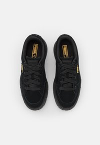 Baskets noires avec une tige en suède, une semelle rembourrée et des coutures texturées. Présentent un logo doré et noir sur la languette et le côté.