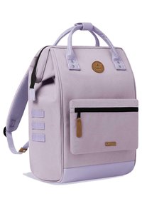 Sac à dos violet clair en tissu, doté de doubles poignées, d'une poche avant zippée et de sangles latérales. Orné d'une étiquette de logo marron.