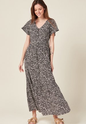 Robe maxi à motif floral noir et blanc, avec un décolleté en V, des manches courtes et flottantes, et une silhouette fluide en tissu léger.