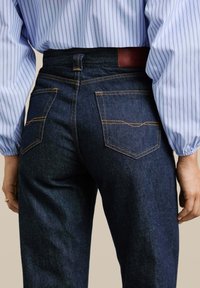 Donkerblauwe spijkerbroeken van denim met oranje stiksels, voorzien van een middelhoge taille, twee achterzakken en een leren label op de tailleband.
