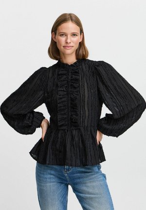 Black blouse with ruffled stripes, high neckline, and balloon sleeves. Lightweight fabric with a peplum shape, paired with blue jeans.