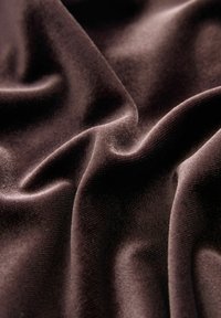 Tamsiai rudos spalvos aksominė medžiaga su minkštu, tekstūruotu paviršiumi, rodanti švelnias raukšles ir glotnią spindesį.