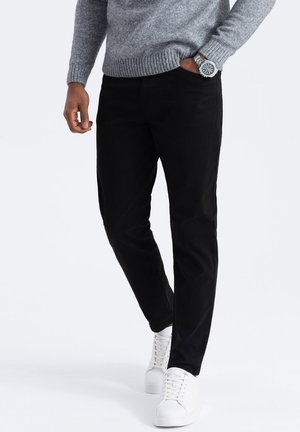 Pantalones negros ajustados de mezcla de algodón, combinados con un suéter gris de punto y zapatillas blancas, con tejido texturizado y un diseño ceñido.