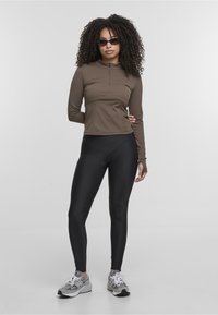 Brown, long-sleeve zip-up top paired with high-waisted black leggings, accented by fitted design. Finished with gray sneakers.