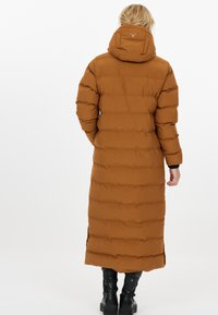 Brun lång pufferjacka med huva, med ett kviltat mönster, sidofickor och en logotyp på ryggen. Ärmarna är något uppblåsta.