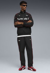 Schwarze Trainingsjacke und -hose mit roten Akzenten und dem Text "Formula 1". Mit Reißverschluss und gerippten Bündchen. Gestreifte Sportschuhe in Rot- und Rottönen.