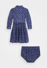 Mörkblå klänning med vitt blommönster, knappad krage, långa ärmar och draperad kjol; inkluderar matchande byxor.