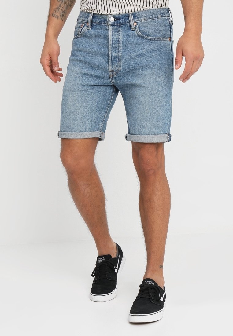 Světlé modré denimové šortky s ohrnutými okraji, s klasickým designem pěti kapes a zapínáním na knoflík. Kombinované s černými nízkými teniskami.