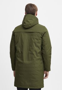 Ol�īvu zaļa parka ar kapuci, izgatavota no gludas, ūdensnecaurlaidīgas auduma, ar garām piedurknēm un vidēju garumu. Minimalistiska apdare.