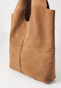 Bruine suède tote bag met een gestructureerd oppervlak, voorzien van geweven details langs de naad en een grote opening aan de bovenkant.