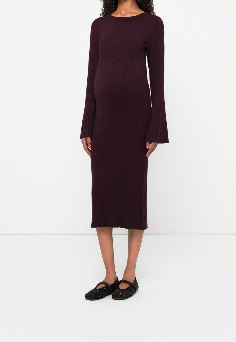 Femme portant une robe midi violet foncé côtelée, à manches longues, avec des poignets évasés et des chaussures plates noires tissées avec des brides.