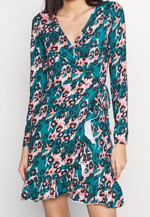 Kvinde iført en langærmet, teal omslagskjole med pink og sort leopardprint og flæsekant, bundet i taljen.