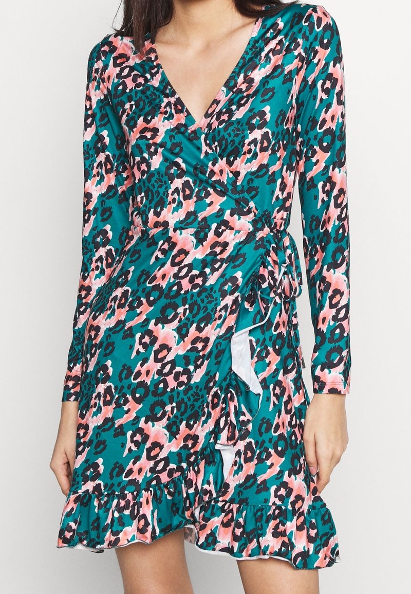 Femme portant une robe portefeuille à manches longues, bleu sarcelle, imprimé léopard rose et noir avec un ourlet volanté, nouée à la taille.