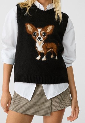 Gilet en tricot noir avec un motif de chihuahua en marron et blanc, porté par-dessus une chemise blanche, assorti à une mini-jupe à carreaux.