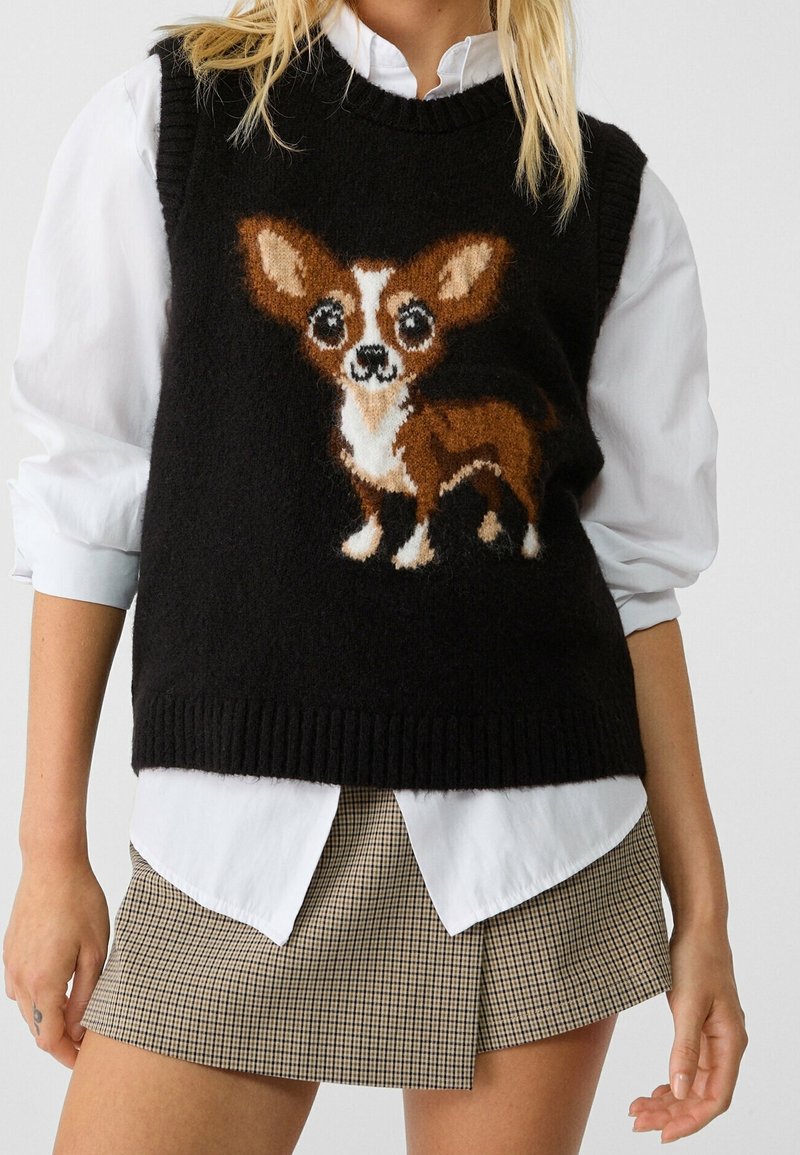 Gilet en tricot noir avec un motif de chihuahua en marron et blanc, porté par-dessus une chemise blanche, assorti à une mini-jupe à carreaux.