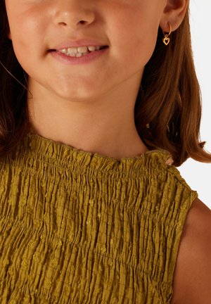 Robe verte texturée avec des détails smockés, présentant un col échancré. Une boucle d'oreille en forme de cœur doré ajoute une touche subtile.