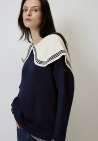 Tumed sinine kudumisse sweater, millel on valge krae siniste triipudega. Sweateril on pikad varrukad ja lõdva istuvus ning pehme tekstuur.