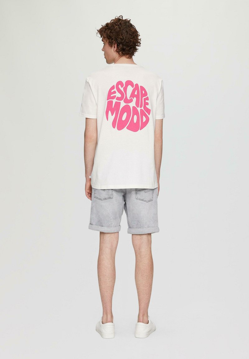 Weißes Baumwoll-T-Shirt mit großem pinkem "ESCAPE MOOD"-Grafik auf dem Rücken, kombiniert mit hellgrauen Shorts und weißen Sneakers.