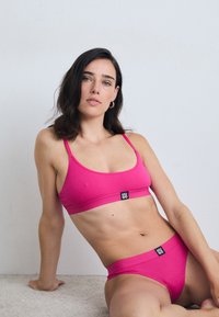 Rosa ribbet bralette og matchende truse med svart logo-merke. Stoffet er glatt og tettsittende, med justerbare stropper.