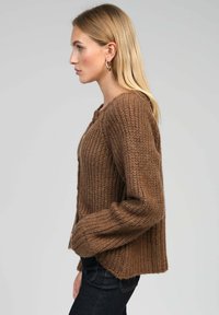 Cardigan en tricot marron avec une coupe décontractée, doté d'un col rond et d'une texture côtelée. Détails de boutons à l'avant et manches longues.