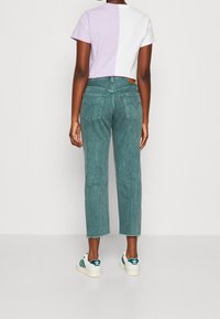 Persona con jeans cortos en tono aguamarina con dobladillos deshilachados, una camiseta de mangas cortas mitad lila mitad blanca, y zapatillas Adidas blancas con rayas verdes.