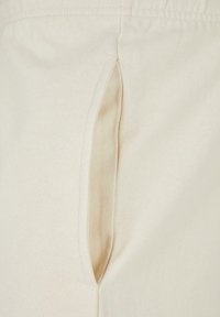 Gros plan sur une poche latérale ouverte d'un pantalon en tissu beige avec des coutures visibles et une texture lisse.