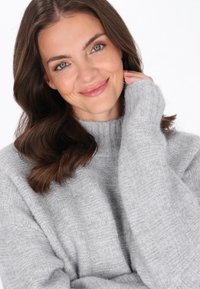 Hellgrau gestrickter Pullover mit hohem Kragen, gerippten Bündchen und einem strukturierten Muster. Weicher Stoff legt sich lässig über die Schultern.