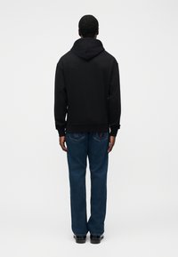 Μαύρο φούτερ με κουκούλα, άνετη εφαρμογή και ριμπ μανσέτες, συνδυασμένο με μπλε τζιν παντελόνι ίσιας γραμμής, με ραφές στην πίσω τσέπη.