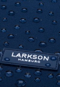 Tissu bleu foncé avec des gouttes d'eau et une étiquette portant la mention "Larkson Hamburg" en texte blanc.